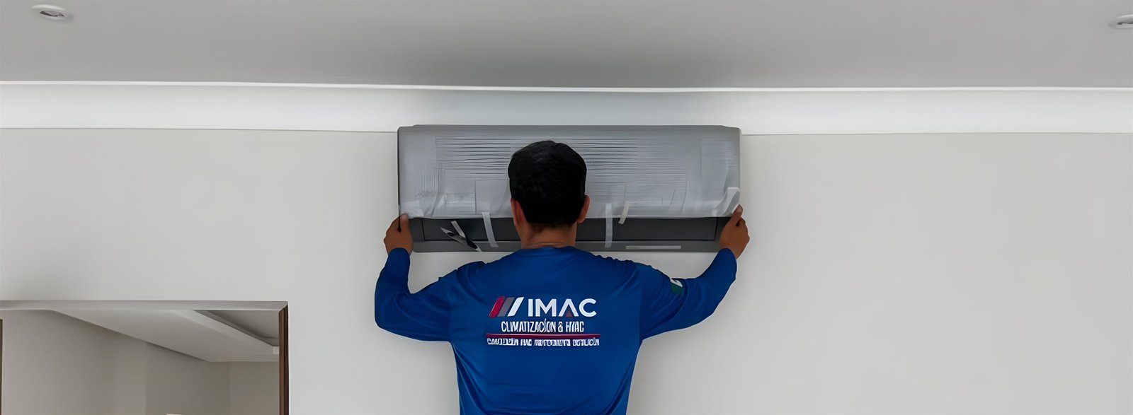 Técnico de IMAC, de espaldas y con el uniforme de la empresa, colocando la unidad interior de un minisplit